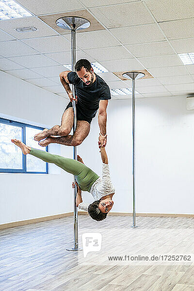 Multiethnische männliche und weibliche Akrobaten üben gemeinsam an einer Stange im Tanzstudio
