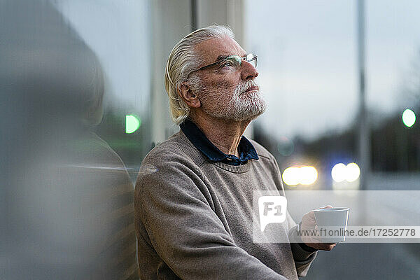 Contemplating senior man with coffee cup outside cafe at street