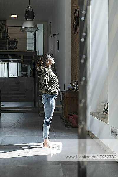 Young woman standing in sunlight at home