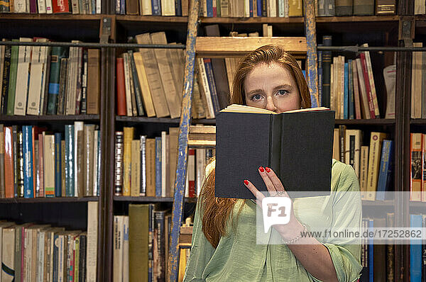 Junge Frau mit Buch auf Leiter in Bibliothek stehend