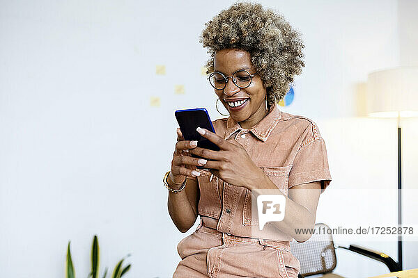 Lächelnde Unternehmerin bei der Nutzung eines Smartphones im Home Office
