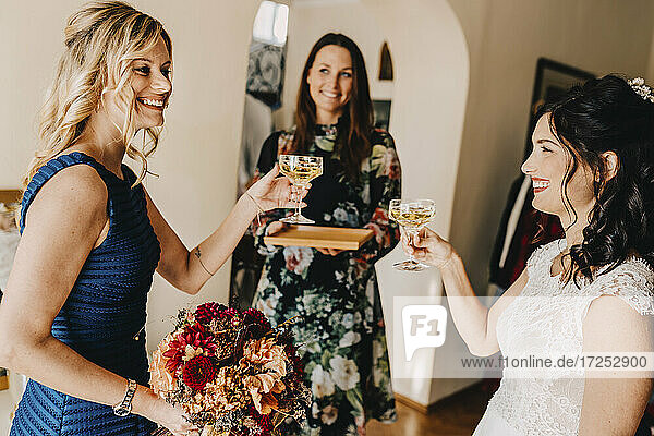 Glückliche Braut mit weiblichen Freunden trinken Wein in häuslichen Raum