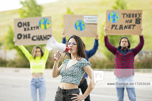 Weibliche Aktivistin mit Hand an der Hüfte und Megaphon auf dem Fußweg