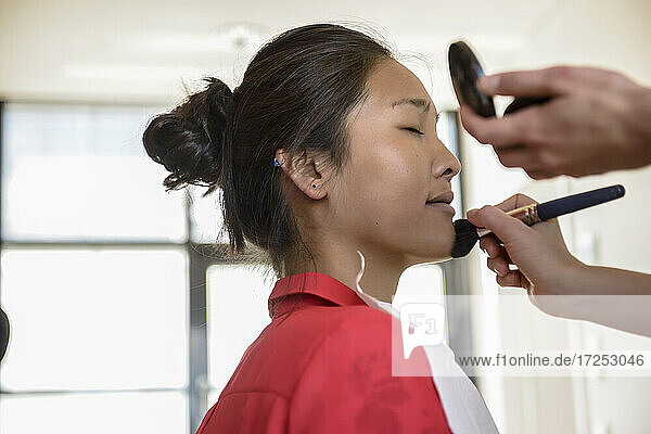 Young make-up artist applying compact powder to female model in studio