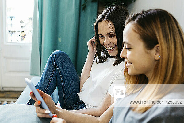 Smiling women sharing mobile phone at home