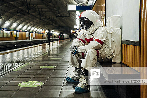 Male astronaut sitting on bench at railway platform