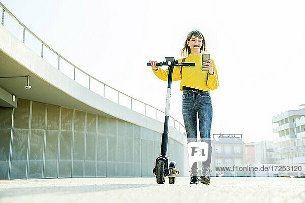 Schöne Frau  die ihr Smartphone benutzt  während sie mit einem Elektroroller spazieren geht