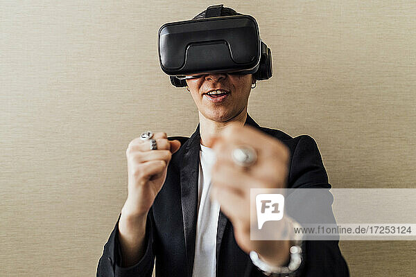 Geschäftsfrau mit Virtual-Reality-Headset  die vor einer Wand steht und gestikuliert