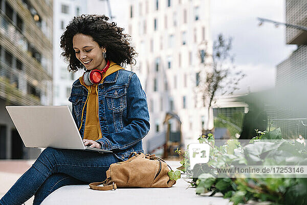 Curly hair woman using laptop while sitting on bench