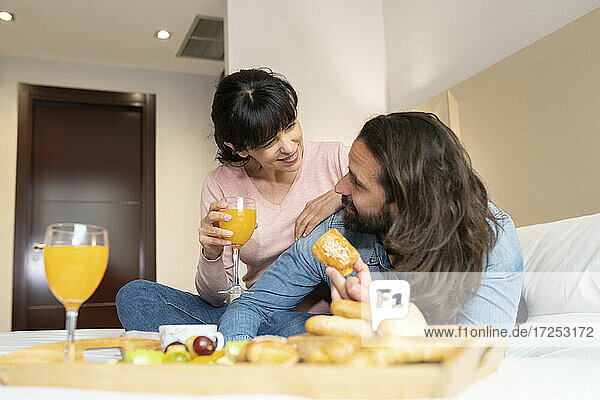 Lächelndes Paar  das sich beim Frühstück auf dem Bett in einer Hotelsuite ansieht