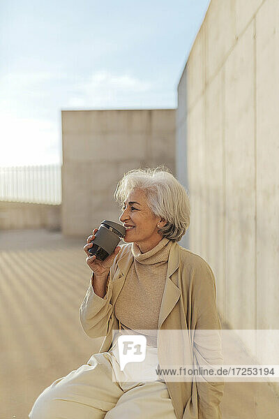 Ältere Frau trinkt Kaffee auf einem Fußweg an einem sonnigen Tag