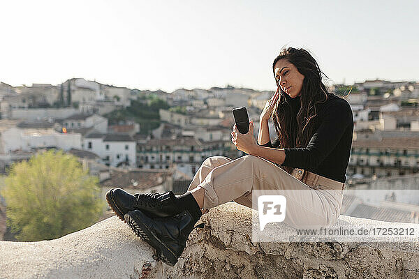 Weibliche Touristin  die ein Selfie mit ihrem Mobiltelefon macht  während sie auf einer Stützmauer sitzt