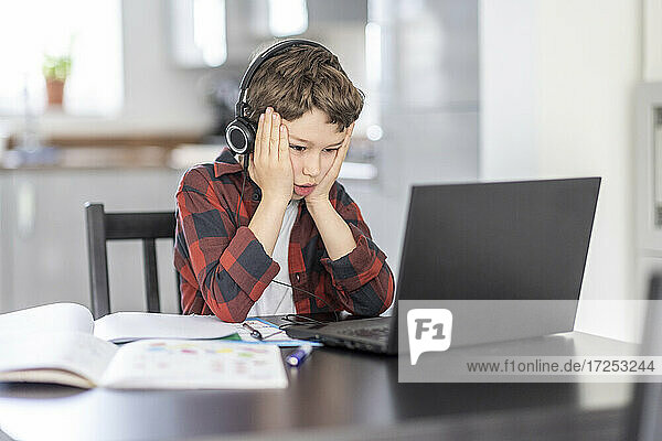 Boy with head in hands studying through laptop at home