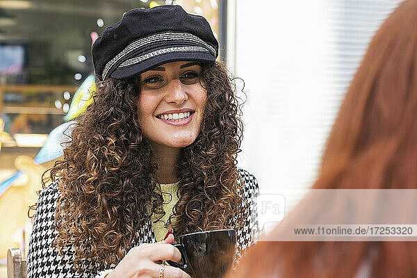Woman wearing cap having coffee with friends at sidewalk cafe