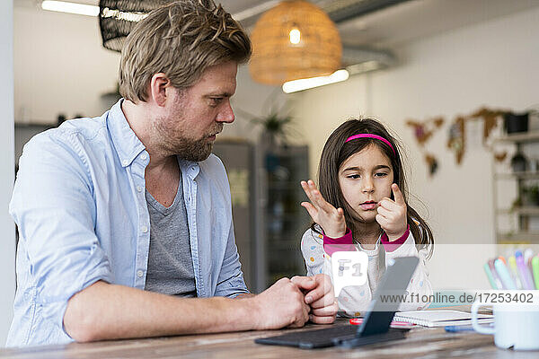 Girl counting fingers while sitting by father at home