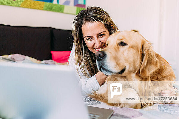 Italien  Junge Frau mit Hund auf dem Bett mit Blick auf den Laptop