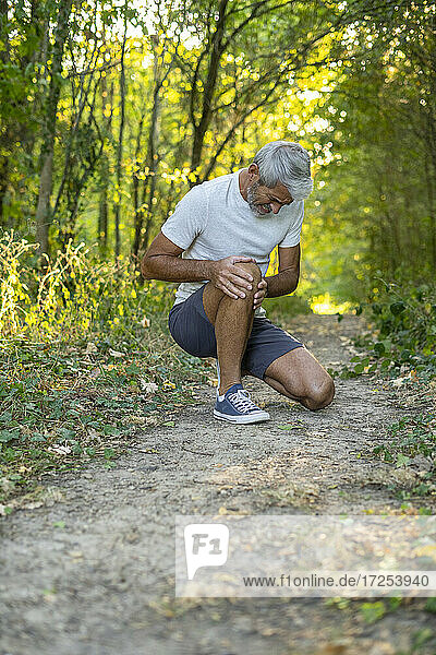 Älterer Mann leidet unter Knieschmerzen  während er im Wald hockt