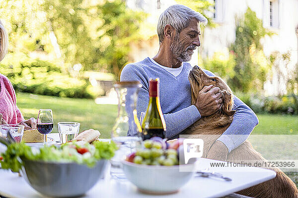 Mature man playing with dog while sitting at table
