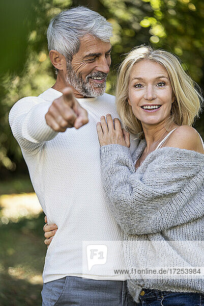 Portrait of smiling mature couple pointing at camera in backyard