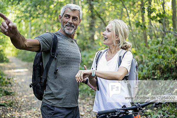Lächelndes reifes Paar  das im Wald die Richtung auf seiner Smartwatch überprüft