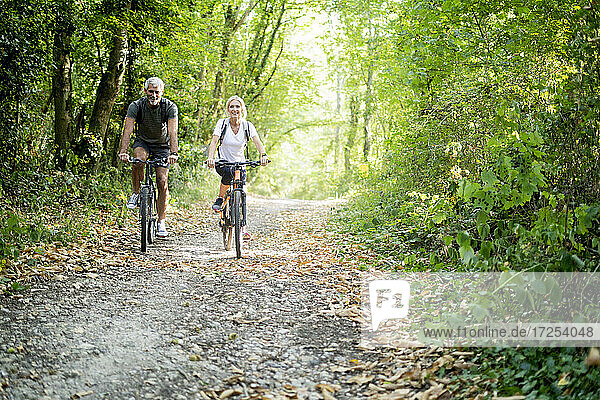 Portrait of smiling mature couple riding bicycles on footpath in forest