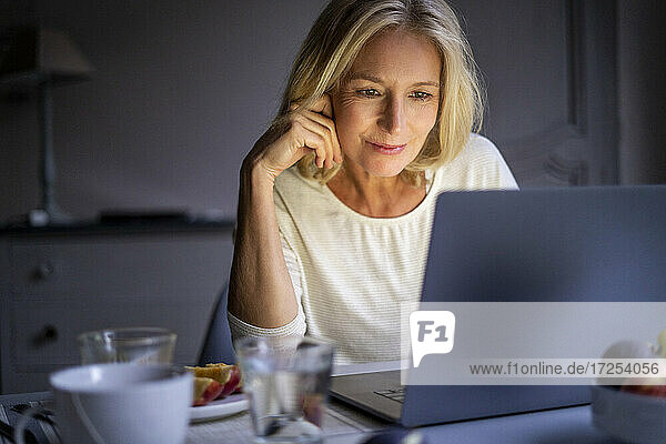 Lächelnde reife Frau benutzt Laptop zu Hause