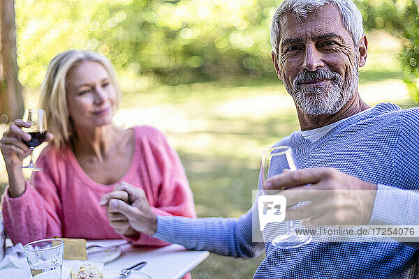 Porträt eines reifen Mannes  der die Hand seiner Frau hält und im Hinterhof Rotwein trinkt