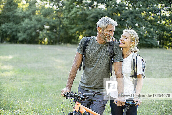 Smiling mature couple with bicycle looking at each other in forest
