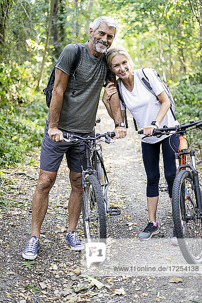 Porträt eines lächelnden reifen Paares mit Fahrrädern  das im Wald steht