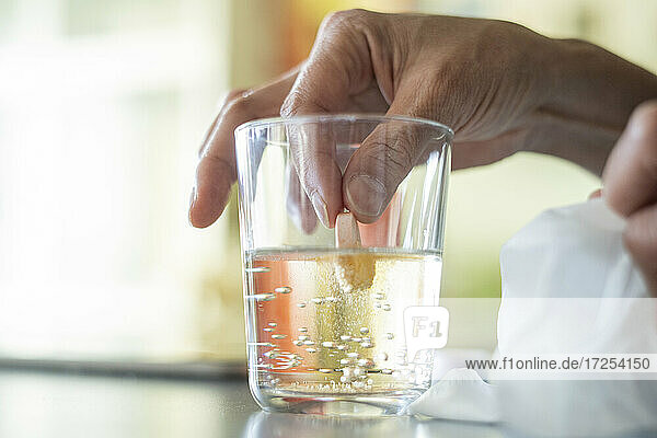Close-up of woman's hand holding pill in glass of water