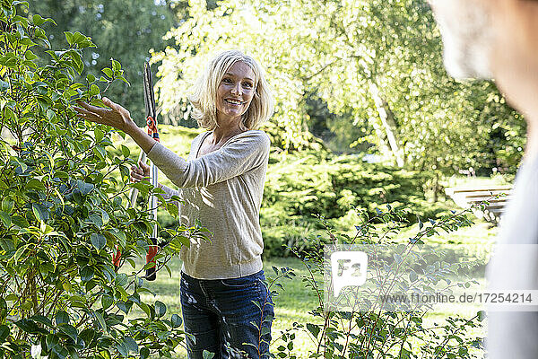 Lächelnde reife Frau mit Gartenschere sieht ihren Mann im Garten an