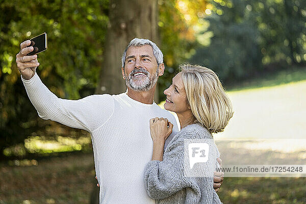 Smiling mature couple taking selfie with smartphone in backyard