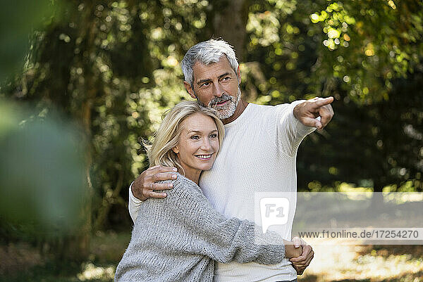 Smiling mature couple pointing while embracing in backyard