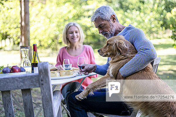 Älterer Mann hält Weinglas und spielt mit Hund im Hinterhof