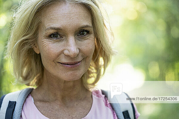 Portrait of smiling mature woman with backpack in forest