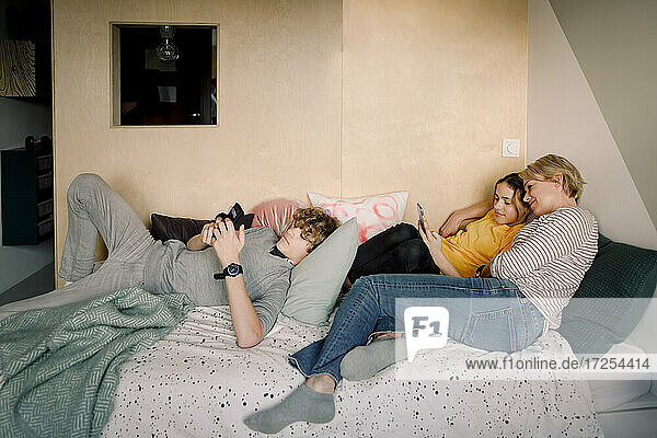 Junge und Mädchen mit Smartphone  während mit Mutter auf dem Bett zu Hause liegen
