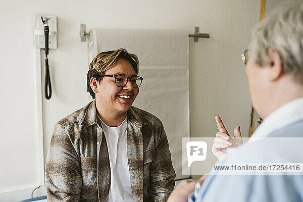 Lächelnde junge männliche Patient Blick auf ältere weibliche Arzt diskutieren in der medizinischen Klinik