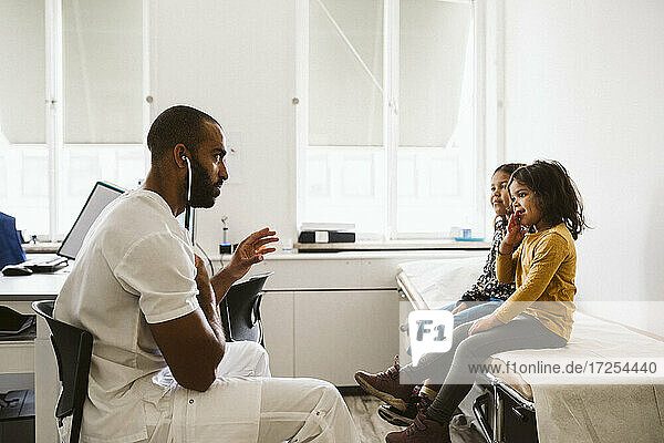 Männlicher Kinderarzt mit Stethoskop gestikulieren  während mit Mädchen Patienten in der medizinischen Klinik sitzen