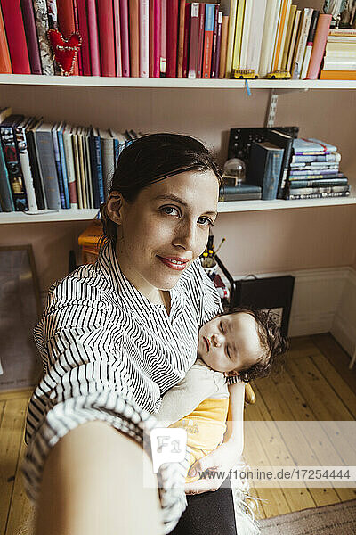 Portrait of mother carrying baby boy while taking selfie at home