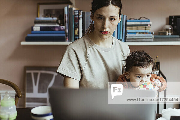 Businesswoman using laptop while sitting with baby boy at home