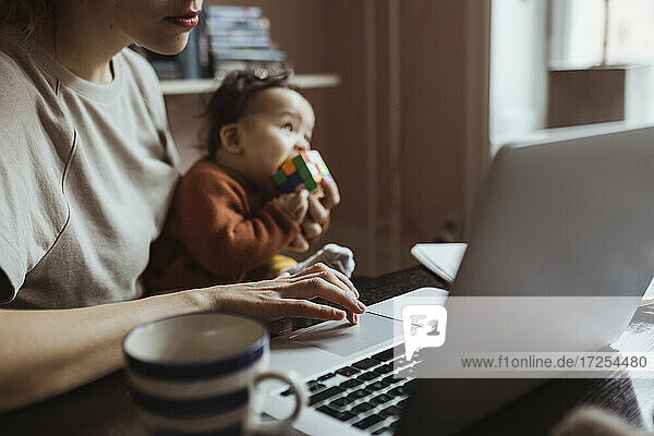 Female entrepreneur with baby boy working on laptop at home office