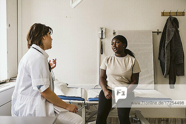 Weiblicher medizinischer Experte  der mit dem Patienten diskutiert  der auf dem Untersuchungstisch in der medizinischen Klinik sitzt