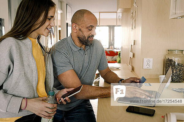 Lächelnd Mädchen Blick auf Vater tun Online-Shopping  während an der Kücheninsel sitzen