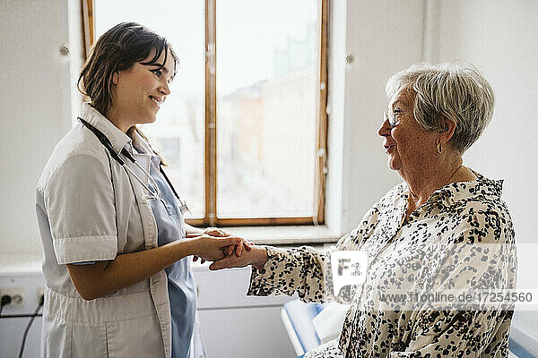 Smiling female healthcare worker looking at senior patient talking while holding hands
