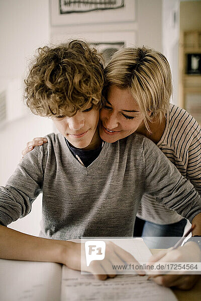 Lächelnde Mutter umarmt Sohn bei den Hausaufgaben