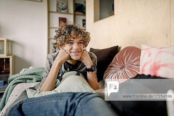 Smiling boy with brown hair lying on bed at home