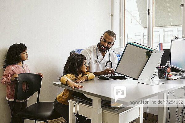 Lächelnder männlicher Kinderarzt im Gespräch mit einem am Schreibtisch sitzenden Mädchen