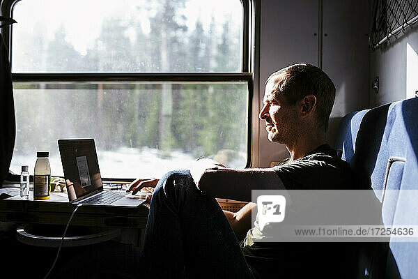 Businessman using laptop while sitting by window in train