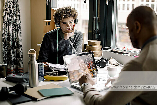 Teenager Junge schaut auf männlichen Unternehmer arbeiten  während am Schreibtisch sitzen