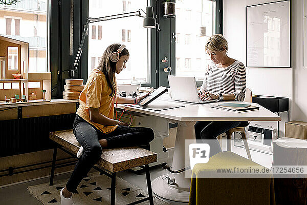 Geschäftsfrau arbeitet  während Tochter zu Hause mit digitalem Tablet lernt